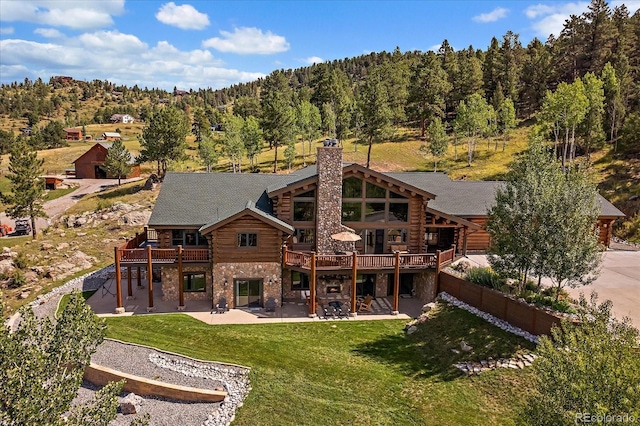 rear view of house with a patio, a lawn, log siding, stone siding, and a forest view