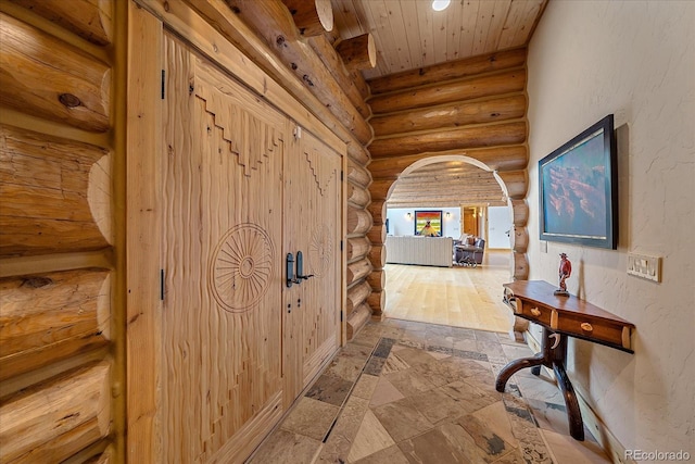 corridor featuring rustic walls, stone tile floors, arched walkways, a textured wall, and wooden ceiling