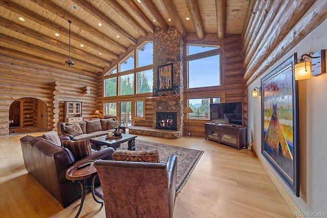 living area featuring light wood finished floors, a stone fireplace, high vaulted ceiling, wooden ceiling, and beamed ceiling