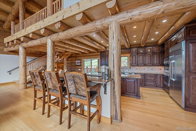 kitchen with wooden ceiling, light wood-style flooring, appliances with stainless steel finishes, log walls, and light stone countertops