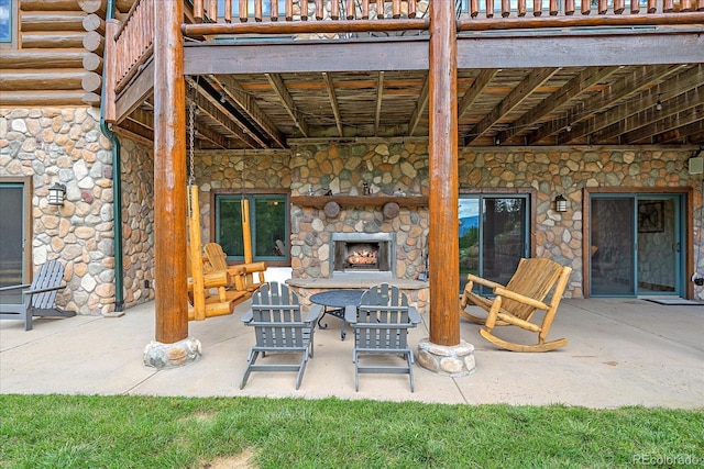view of patio featuring an outdoor stone fireplace and a balcony