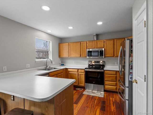 kitchen featuring dark hardwood / wood-style floors, sink, a kitchen bar, kitchen peninsula, and stainless steel appliances