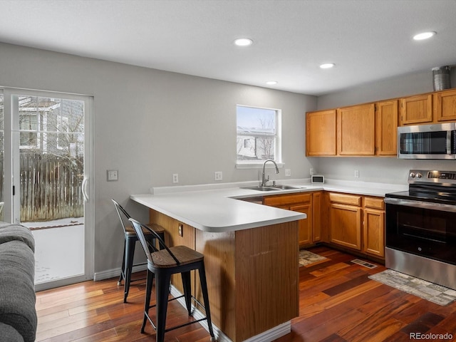 kitchen featuring appliances with stainless steel finishes, a breakfast bar, sink, dark hardwood / wood-style flooring, and kitchen peninsula