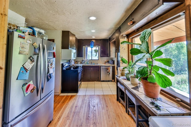 kitchen featuring a textured ceiling, stainless steel appliances, dark brown cabinetry, and light hardwood / wood-style floors