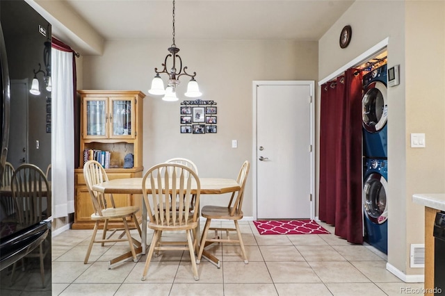 tiled dining area with stacked washing maching and dryer and a chandelier