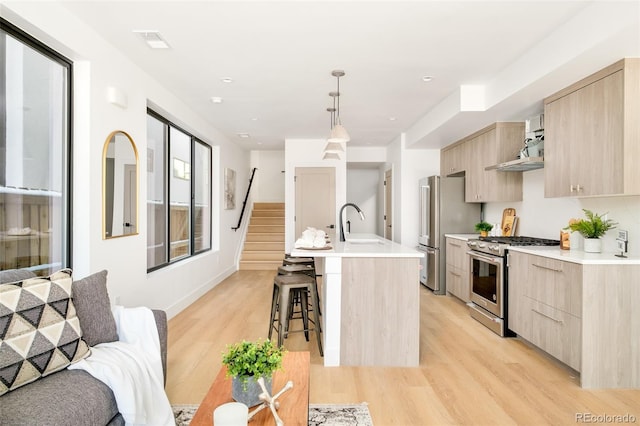 kitchen featuring a breakfast bar area, decorative light fixtures, a center island with sink, light brown cabinets, and appliances with stainless steel finishes