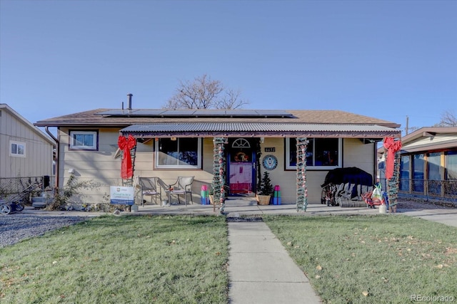 view of front of property featuring a porch, a front lawn, and solar panels