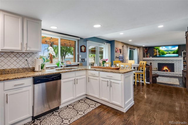 kitchen with a brick fireplace, white cabinetry, dishwasher, and kitchen peninsula