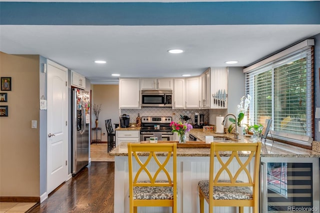 kitchen with kitchen peninsula, a breakfast bar area, appliances with stainless steel finishes, beverage cooler, and sink