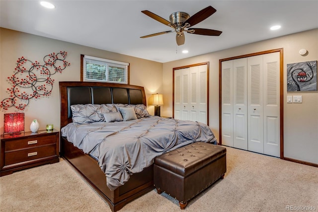 bedroom with ceiling fan, light colored carpet, and multiple closets