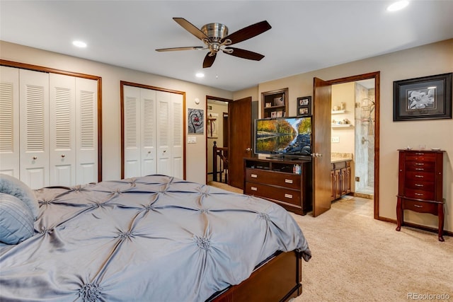 bedroom featuring ceiling fan, ensuite bathroom, light carpet, and multiple closets