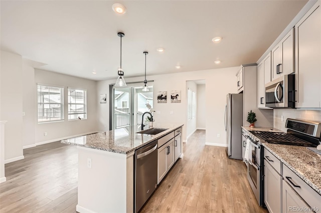 kitchen featuring a sink, an island with sink, light wood-style flooring, baseboards, and appliances with stainless steel finishes