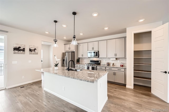 kitchen featuring a sink, a center island with sink, gray cabinetry, appliances with stainless steel finishes, and tasteful backsplash