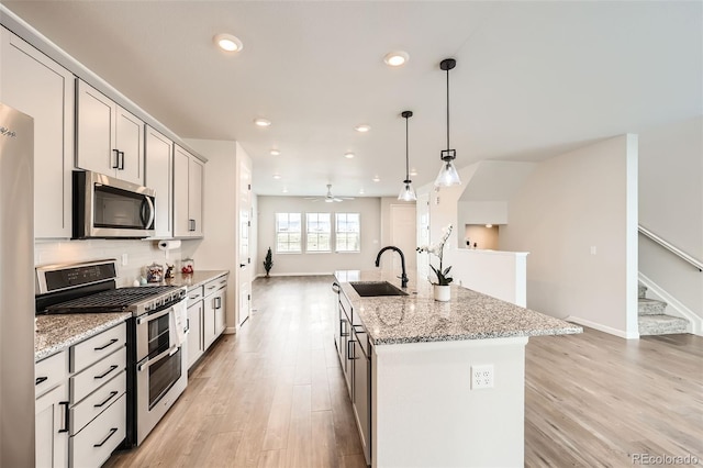 kitchen with stainless steel appliances, a kitchen island with sink, light wood-type flooring, and a sink