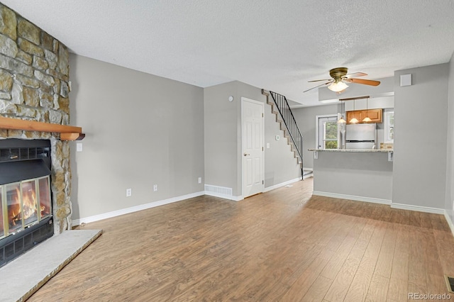 3619 Queen Anne Way, Colorado Springs, CO 80917 - unfurnished living room featuring ceiling fan, a textured ceiling, a fireplace, wood finished floors, and stairway