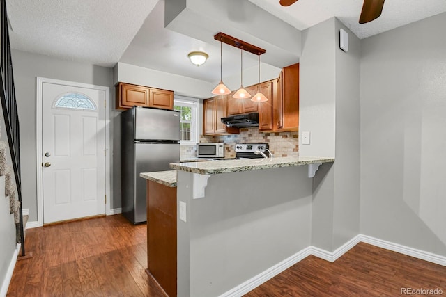 3619 Queen Anne Way, Colorado Springs, CO 80917 - kitchen with freestanding refrigerator, under cabinet range hood, dark wood-type flooring, brown cabinets, and a peninsula