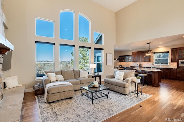 living room with sink, a notable chandelier, light hardwood / wood-style flooring, and a stone fireplace