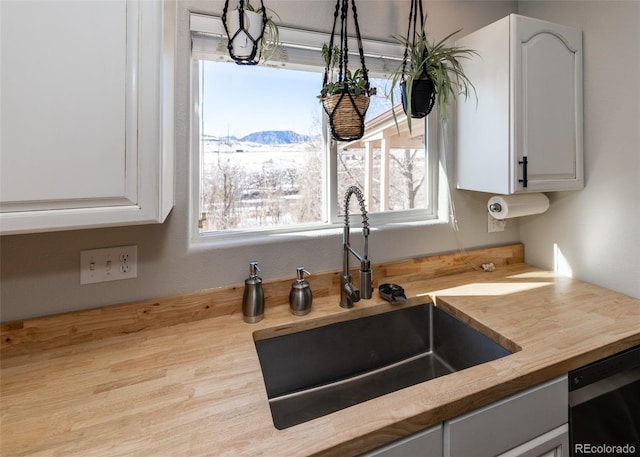 kitchen featuring white cabinetry, wooden counters, black dishwasher, and sink