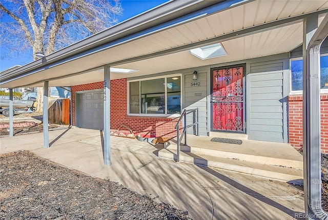 view of exterior entry featuring a porch, brick siding, driveway, and a garage