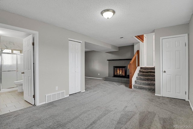 unfurnished living room featuring light colored carpet, a textured ceiling, and a brick fireplace