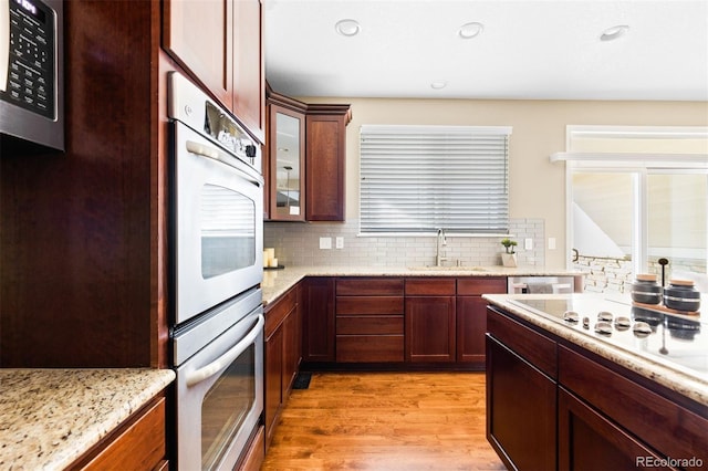 kitchen featuring sink, stainless steel appliances, light stone counters, light wood-type flooring, and tasteful backsplash