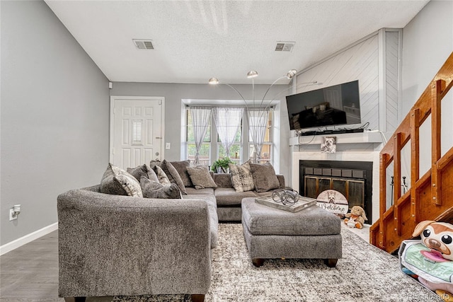 living room featuring visible vents, a fireplace, a textured ceiling, and wood finished floors