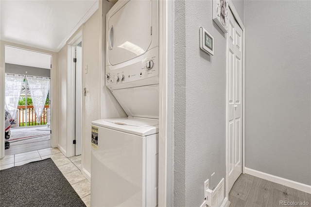 clothes washing area featuring visible vents, light wood-style floors, stacked washer / dryer, laundry area, and baseboards