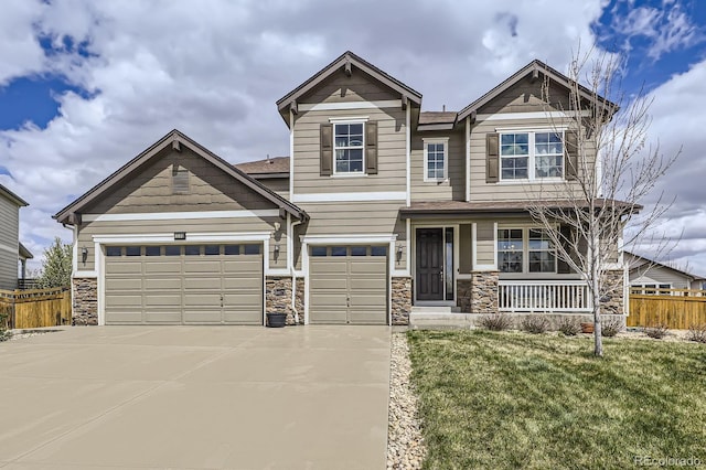 craftsman-style home featuring fence, covered porch, concrete driveway, and stone siding