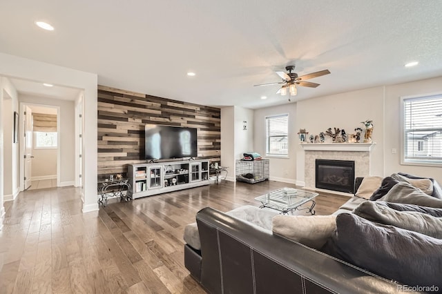 living area featuring wooden walls, a fireplace, an accent wall, a ceiling fan, and baseboards