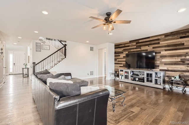 living area with a ceiling fan, visible vents, wood finished floors, stairway, and wooden walls