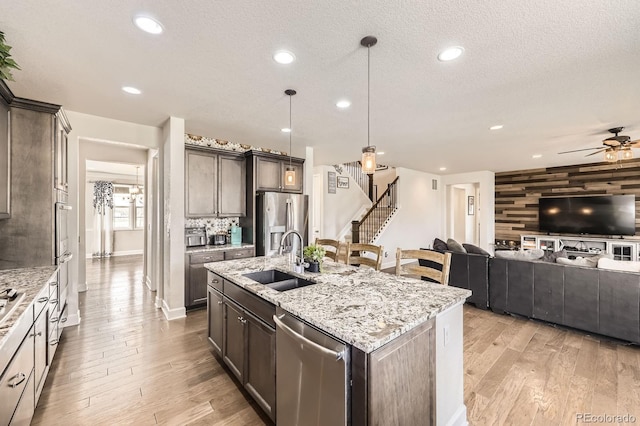 kitchen featuring a ceiling fan, light wood-type flooring, light stone counters, a sink, and stainless steel appliances