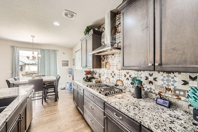 kitchen with an inviting chandelier, dark brown cabinetry, stainless steel appliances, and wall chimney exhaust hood