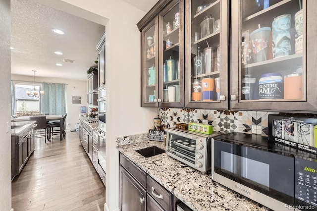 bar with decorative backsplash, hanging light fixtures, a toaster, an inviting chandelier, and light wood-style flooring