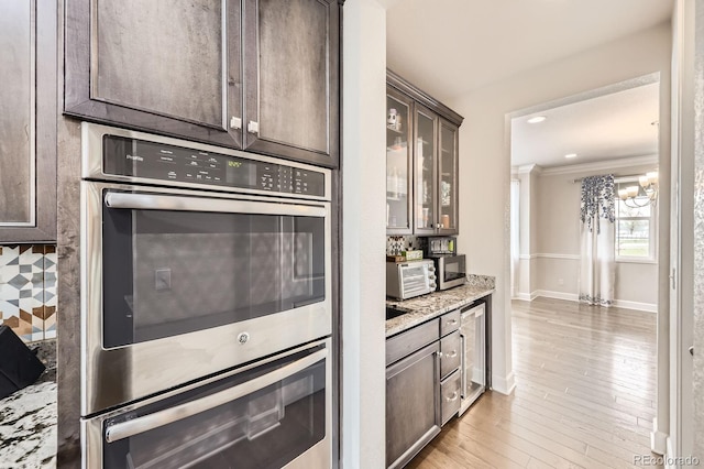 kitchen with crown molding, dark brown cabinets, appliances with stainless steel finishes, a chandelier, and glass insert cabinets