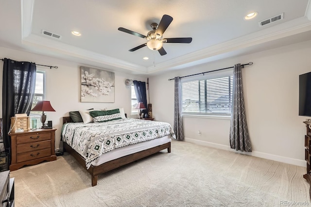 bedroom with multiple windows, visible vents, light carpet, and a raised ceiling