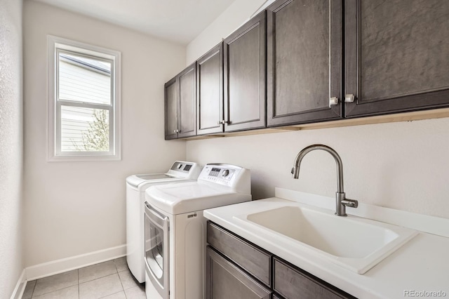laundry area featuring washing machine and dryer, cabinet space, a sink, baseboards, and light tile patterned floors