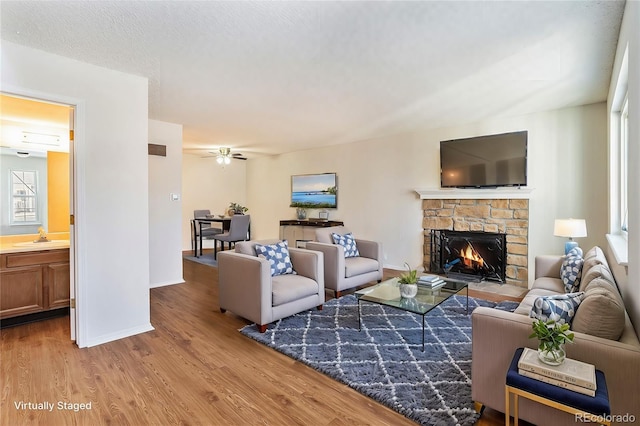 living room featuring sink, a textured ceiling, ceiling fan, a fireplace, and light hardwood / wood-style floors