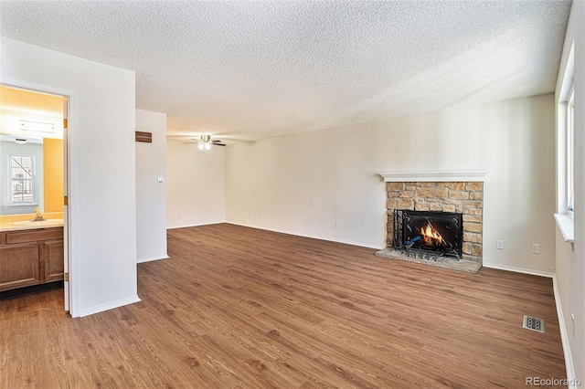 unfurnished living room featuring sink, ceiling fan, a textured ceiling, a stone fireplace, and light wood-type flooring