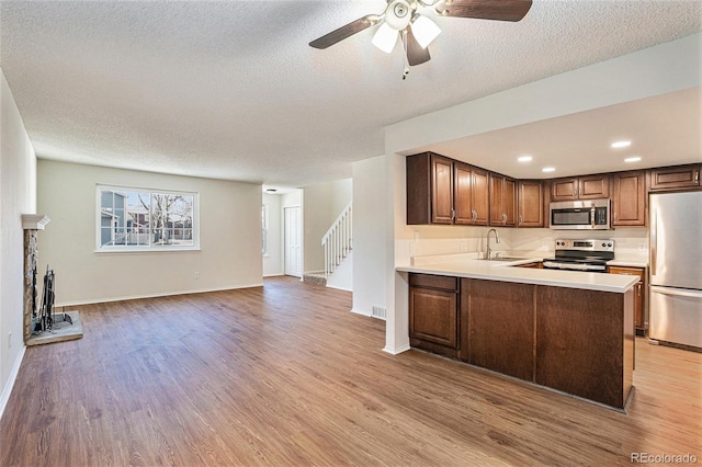 kitchen featuring light hardwood / wood-style flooring, a textured ceiling, appliances with stainless steel finishes, kitchen peninsula, and a fireplace