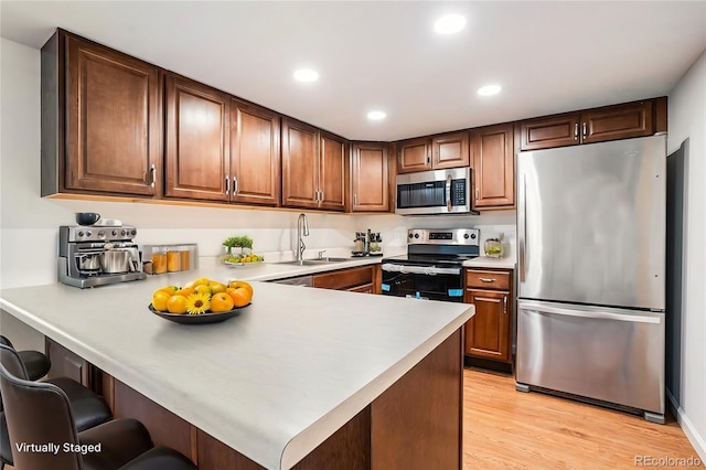 kitchen with sink, light wood-type flooring, a kitchen breakfast bar, kitchen peninsula, and stainless steel appliances