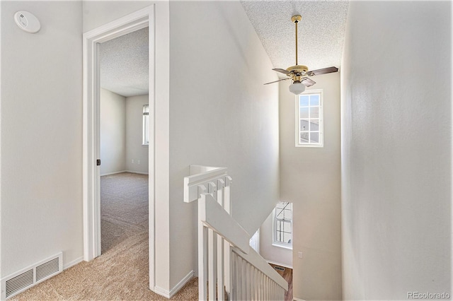 hall with light colored carpet and a textured ceiling