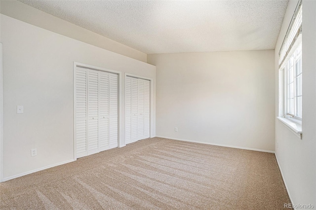 unfurnished bedroom with carpet flooring, two closets, and a textured ceiling