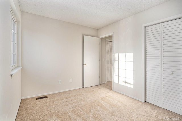 unfurnished bedroom featuring light carpet, a closet, and a textured ceiling