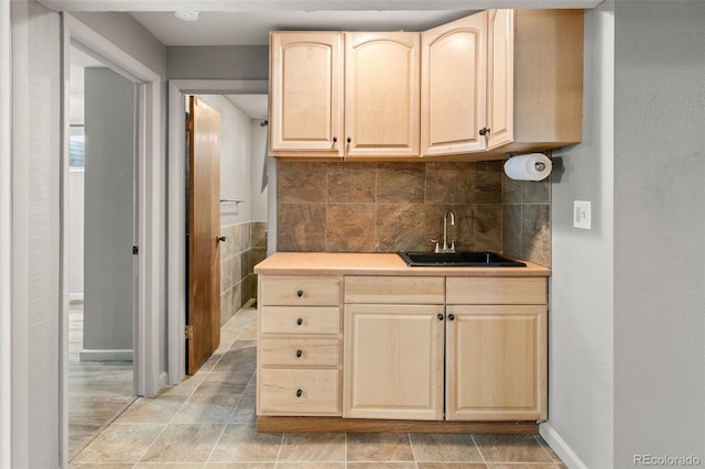 kitchen with backsplash, light brown cabinetry, a sink, baseboards, and light countertops