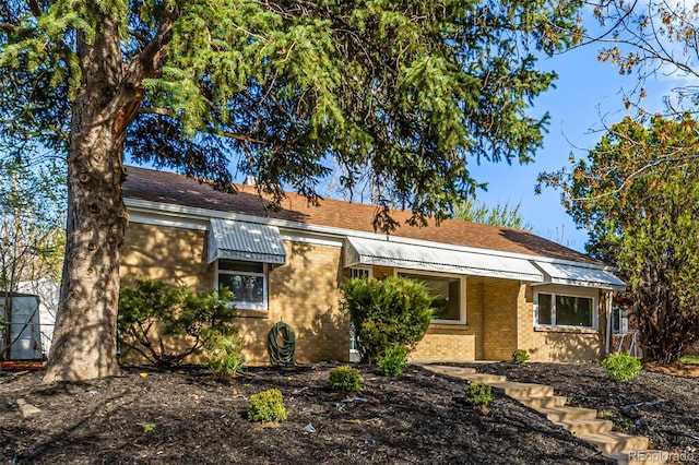 ranch-style home featuring roof with shingles and brick siding