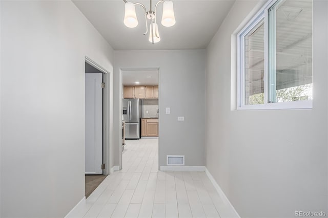 hallway with a notable chandelier, visible vents, and baseboards