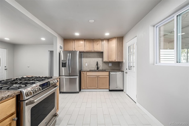 kitchen with dark stone counters, recessed lighting, appliances with stainless steel finishes, a sink, and decorative backsplash