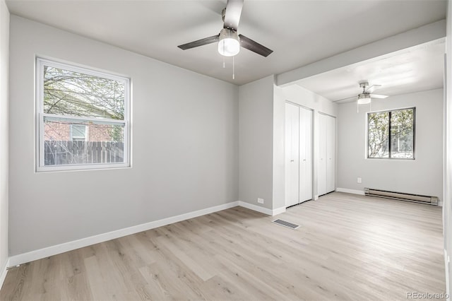 unfurnished bedroom featuring two closets, light wood-style flooring, visible vents, baseboard heating, and baseboards