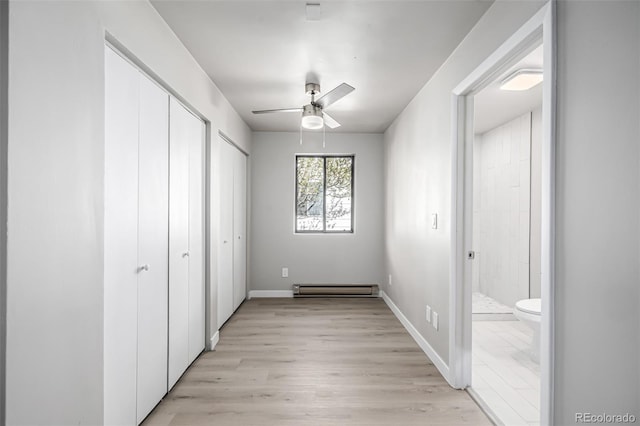 unfurnished bedroom with light wood-style floors, ceiling fan, ensuite bath, multiple closets, and a baseboard radiator