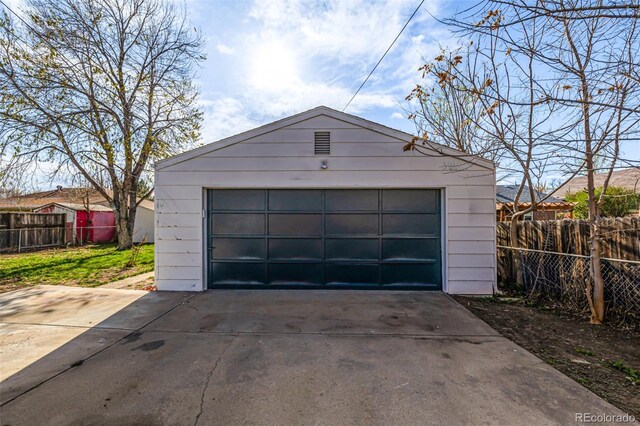 detached garage featuring concrete driveway and fence